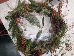Festive holiday wreath lying on a table, adorned with red and yellow berries as well as pinecones