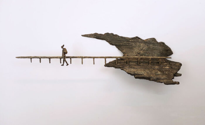 Sculpture by Varvara Mitrofanova depicting a person walking along a fence away from a rocky landscape