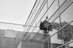 The artist Matt Witmer attached by a harness to the side of a building covered with large glass windows