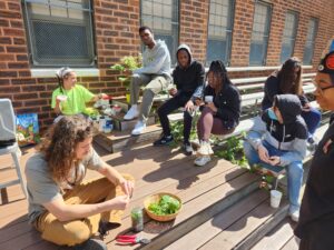 Our two educators sitting on the left, prepping our meal, while the Saul High School students sit on the bleachers on the right, discussing the process of cooking with foraged foods