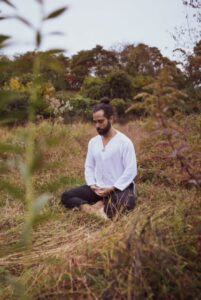 Yoga instructor Noah Julian sitting tranquilly, looking down, in an amber-colored autumn meadow.