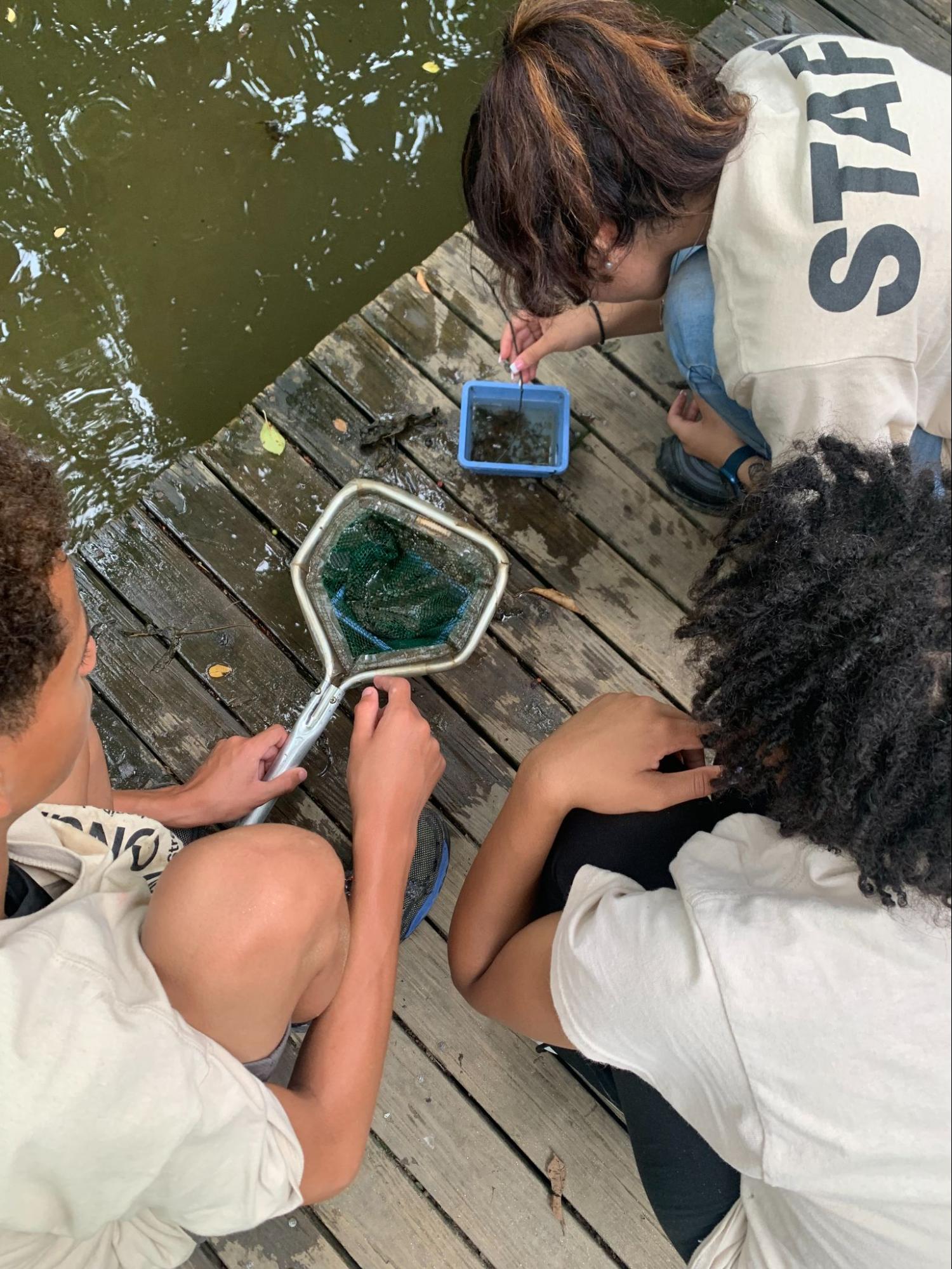 A few students with an instructor as they examine contents retrieved by a net from the water