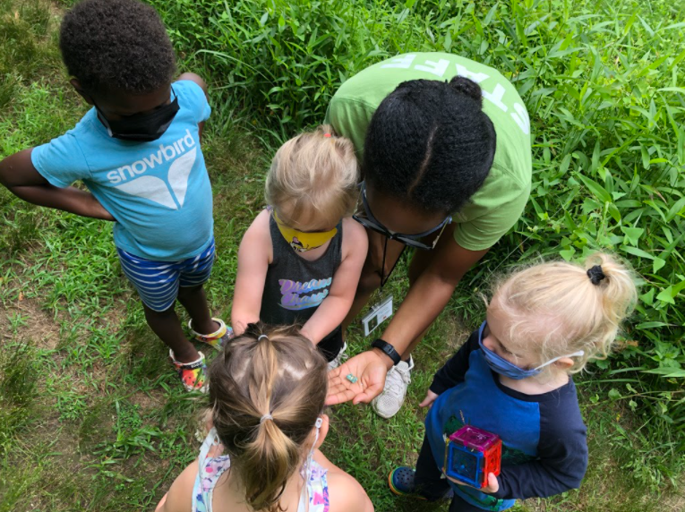 A few children looking at nature objects a teacher and other child are holding